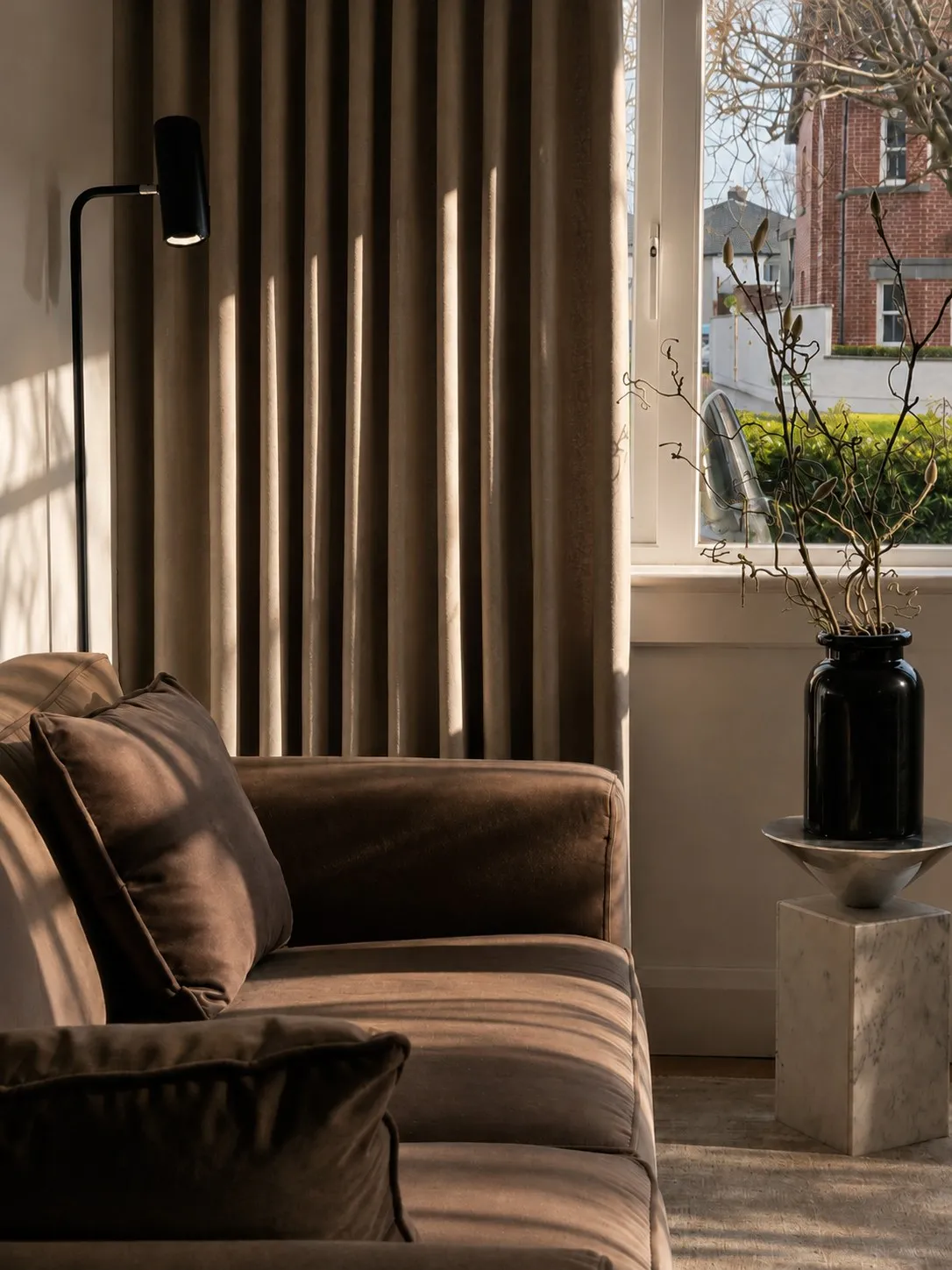 Velvet sofa beside the window with a dark vase and winter branches